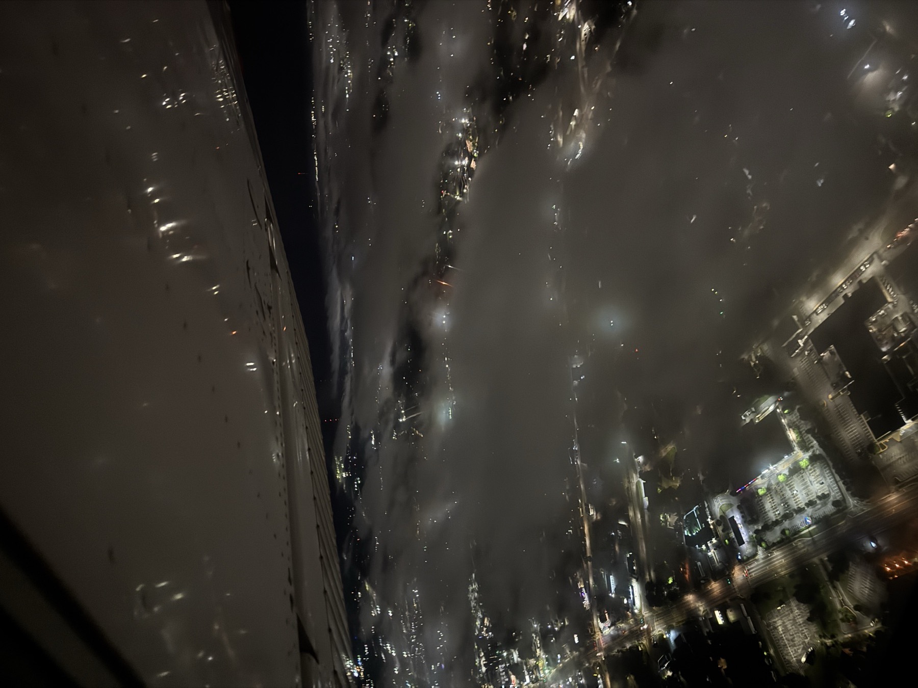 City lights of Columbus glowing through a cloud layer below the wing at night